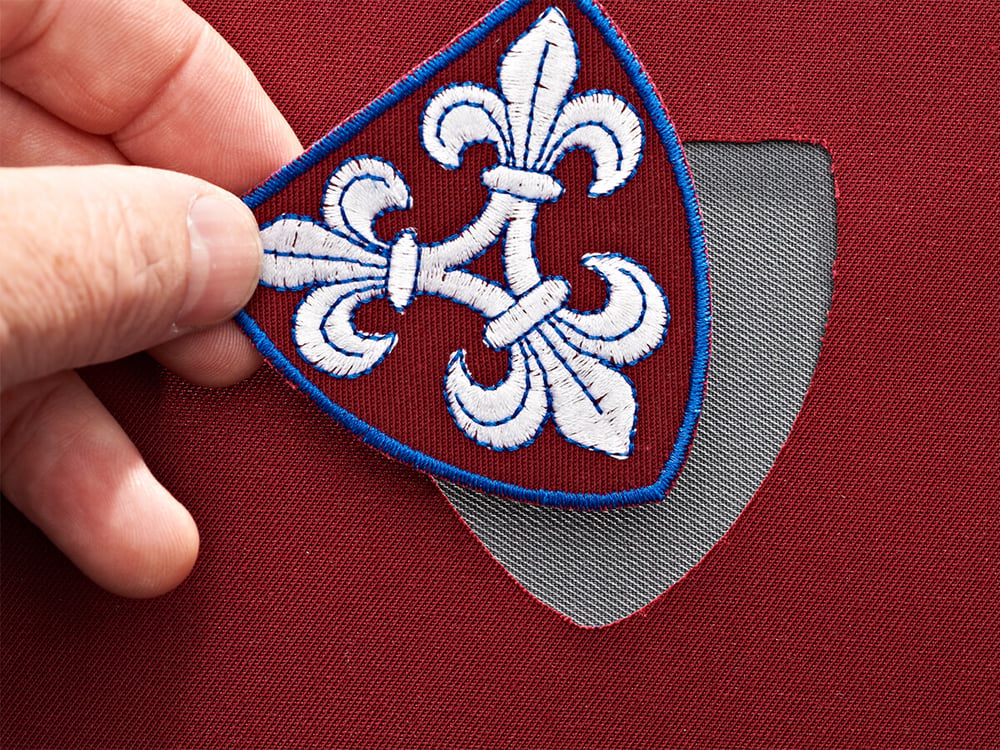 Gesticktes Wappen-Emblem mit Lilienmotiv, aufgebracht auf Stoffpatch – Beispiel aus der Arbeit bei KinzigStick
